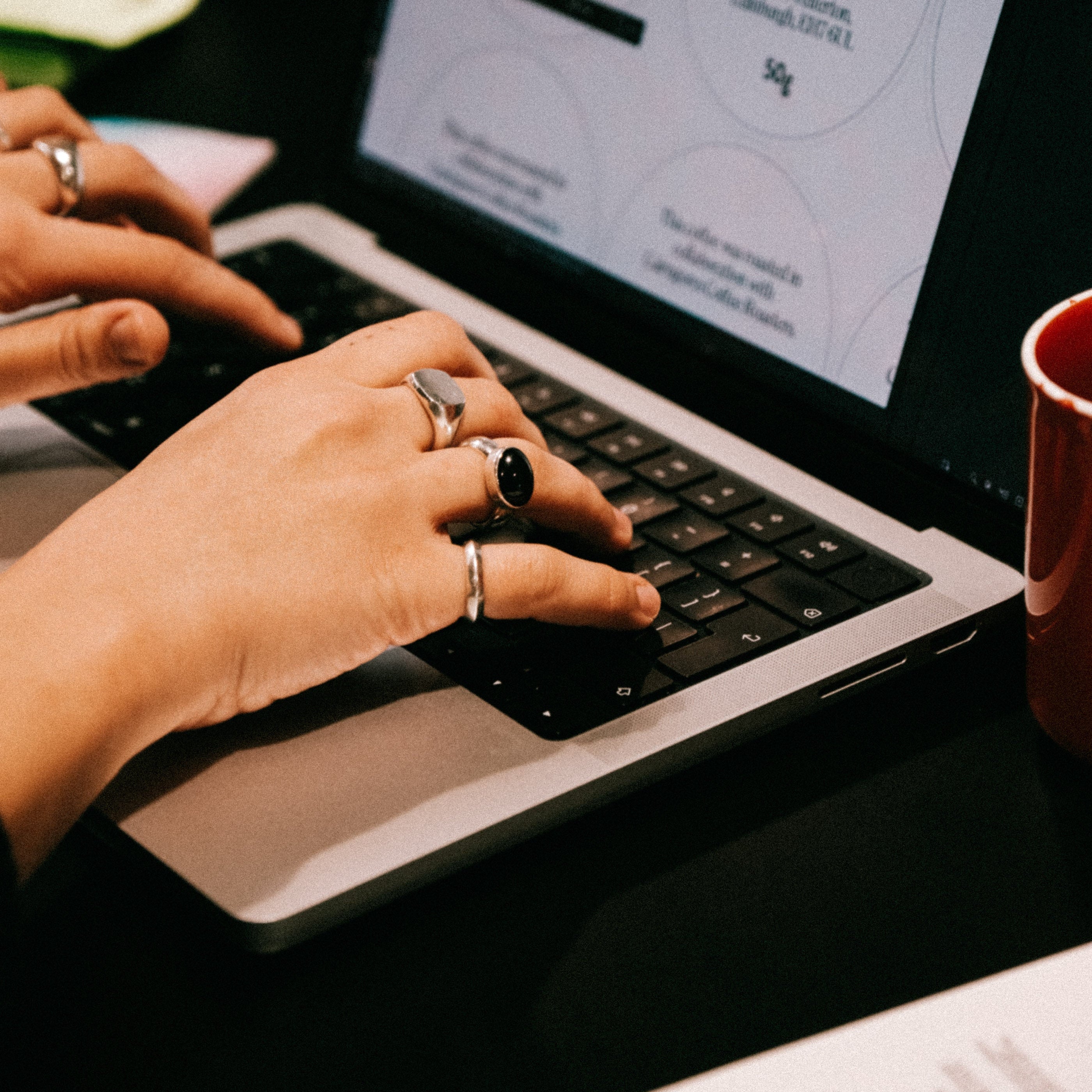 Person typing on a laptop with a mug and paper in the background